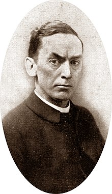 Black and white photograph of clean-shaven white man of middle age, with short dark hair, wearing clerical dress