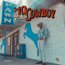 A man wearing a white cowboy hat, patterned shirt and white pants leaning against the white brick exterior wall of a pawn shop, with the title superimposed.