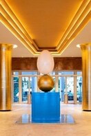 A giant cracked egg sculpture stands above a golden orb, both are supported by a blue cube