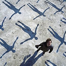 A man standing on a sidewalk among the shadows of figures above