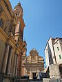 À gauche de la photo, la façade de style baroque de la basilique Saint-Michel-Archange (consacrée en 1675) au cœur de la vieille ville de Menton, au-dessus du parvis saint Michel pavé de galets noirs et blancs aux armes des Grimaldi. Son campanile, au flanc droit, élève sa coupole à 53 mètres de hauteur. Au fond, nous fait face la Chapelle de l'Immaculée-Conception ou Chapelle des Pénitents blancs.