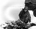 T/Sgt. Harry A. Downard, San Diego, Calif., Signal Corps Photographer, holds up leather thong which was used to tie the legs and coat of this paratrooper 101st Airborne Division, who was killed near Bastogne, (01/12/1945)