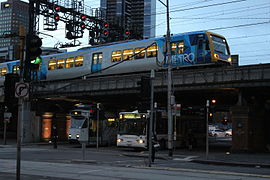 Yarra Trams Z-class tram beside a Melbourne Bus Link Scania bus, with a Metro Trains X'Trapolis 100 passing above