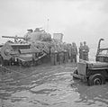 German prisoners wait for collection in the shadow of a disabled Sherman Crab flail tank, 6 June 1944.