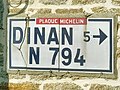 Une plaque émaillée Michelin, indiquant la ville de Dinan à 5 kilomètres sur la route de Corseul (D794), scellée sur le mur d’une maison.