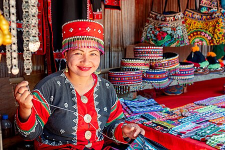 Karen tribal woman in traditional clothes sitting and sewing, in Thailand.