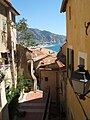 Une magnifique vue d'une ruelle pittoresque du Vieux Menton. En arrière plan, on aperçoit le port de Menton-Garavan avec la frontière italienne au fond à droite.